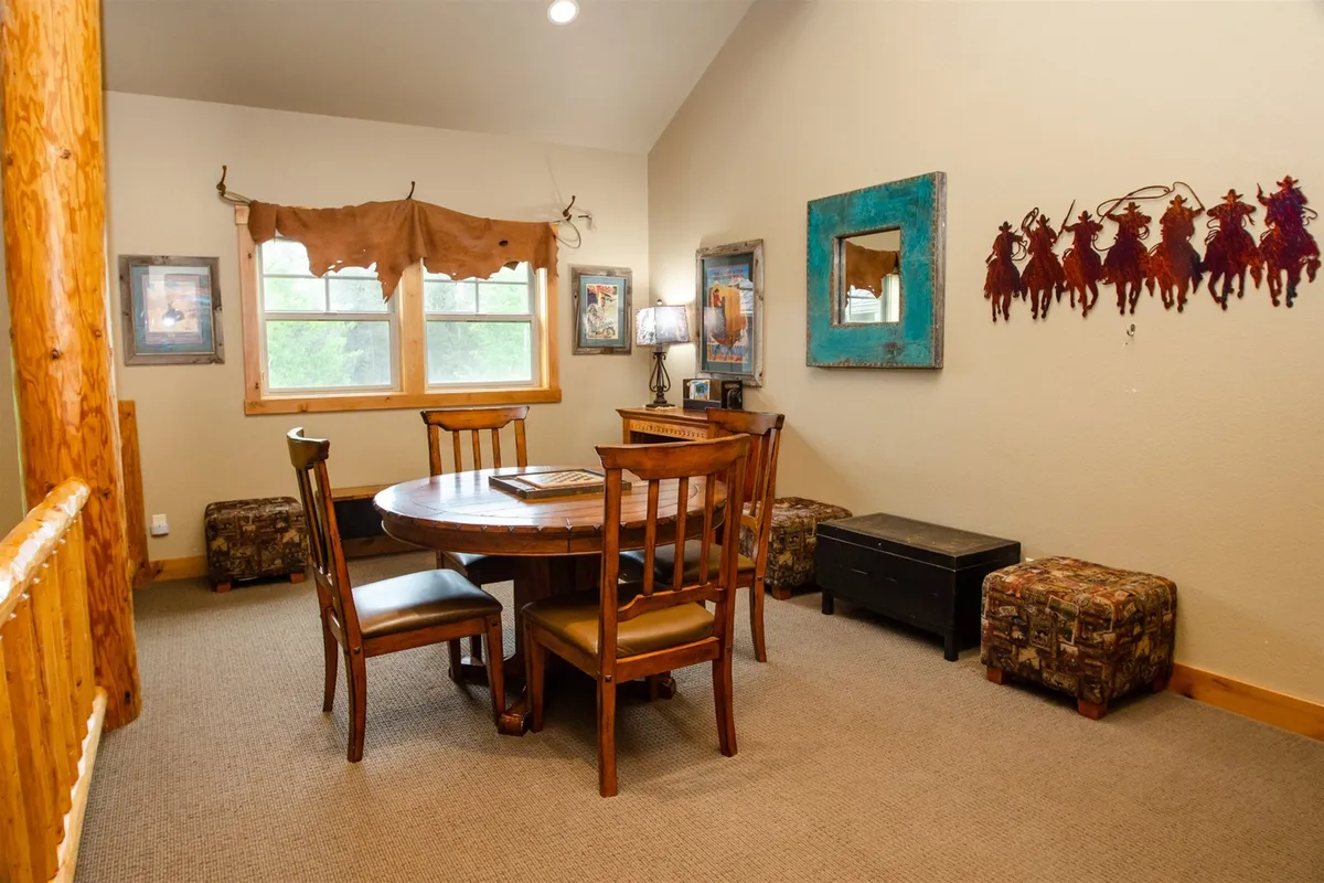 A cozy loft area with a round wooden table, colorful wall art, and unique stools. The space is well-suited for board games, poker nights, or casual conversations. The warm and welcoming atmosphere invites people to gather for fun and friendly competition.