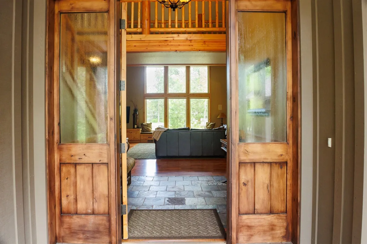 A bright, inviting entryway with double wooden front doors, large windows, and a cozy seating area. Natural wood accents and abundant sunlight create a warm, welcoming atmosphere—ideal for gathering, relaxing, or enjoying the changing seasons from the comfort of home.