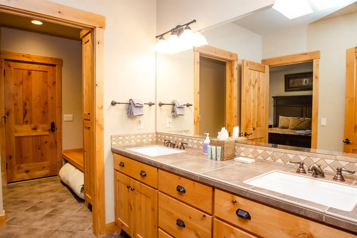 A bright, modern bathroom with a double sink vanity, wooden cabinetry, a mirror, and a bathroom door, bathed in morning light from a skylight. The setting suggests shared moments of grooming and relaxation.