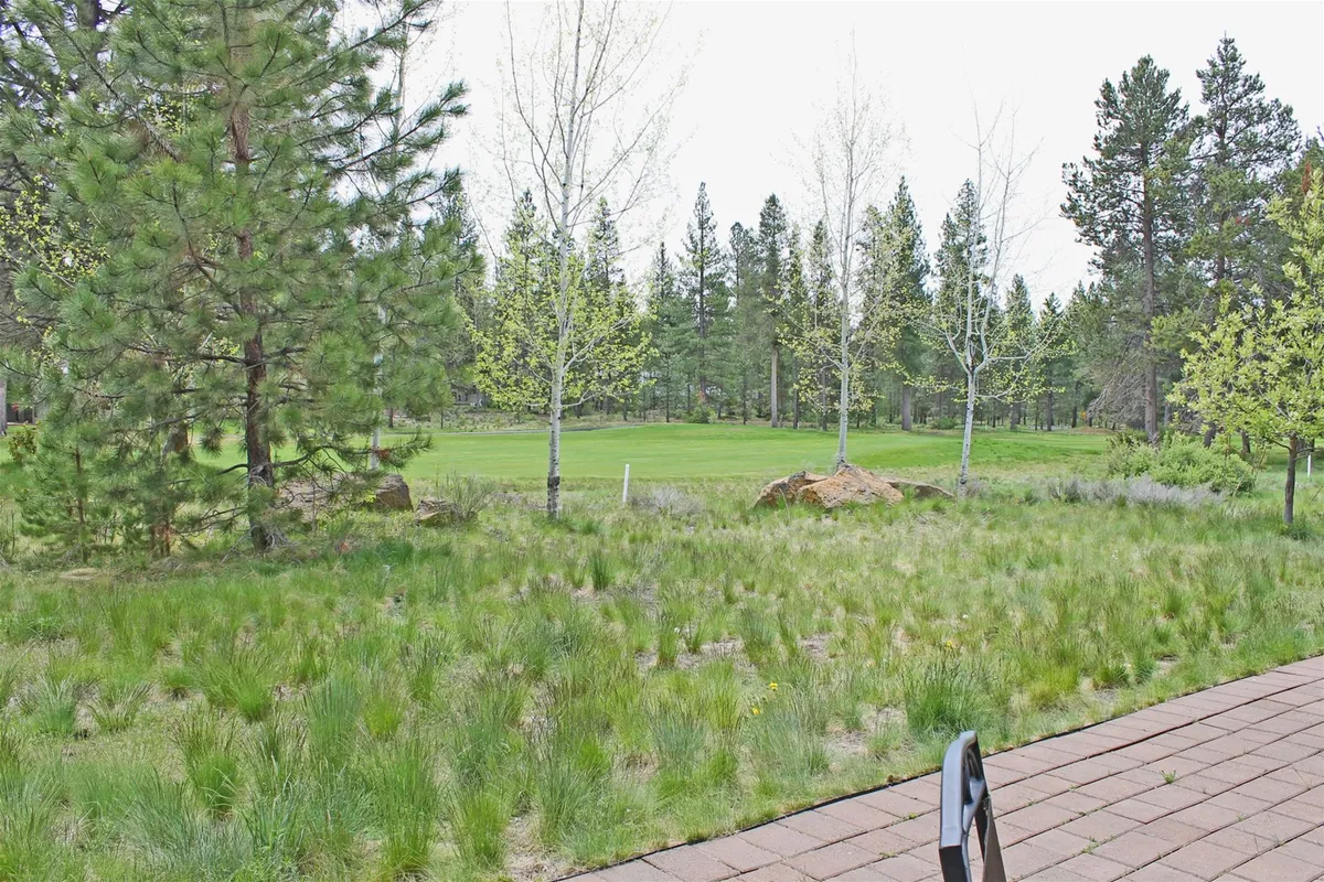 A wide, lush expanse of the golf course surrounded by tall trees and manicured green grass. The view captures the serene landscape of Sunriver, with early morning light casting soft shadows across the rolling fairway. The scene hints at the exclusive access to golfing right outside the retreat and the tranquil environment guests can experience from their private patio.