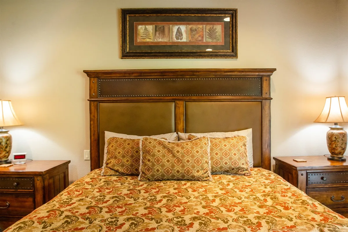 This image captures a serene king suite with a bed adorned with an ornate comforter, decorative pillows, framed artwork, and nightstands with lamps. The space exudes warmth and privacy, perfect for restful nights and relaxation.