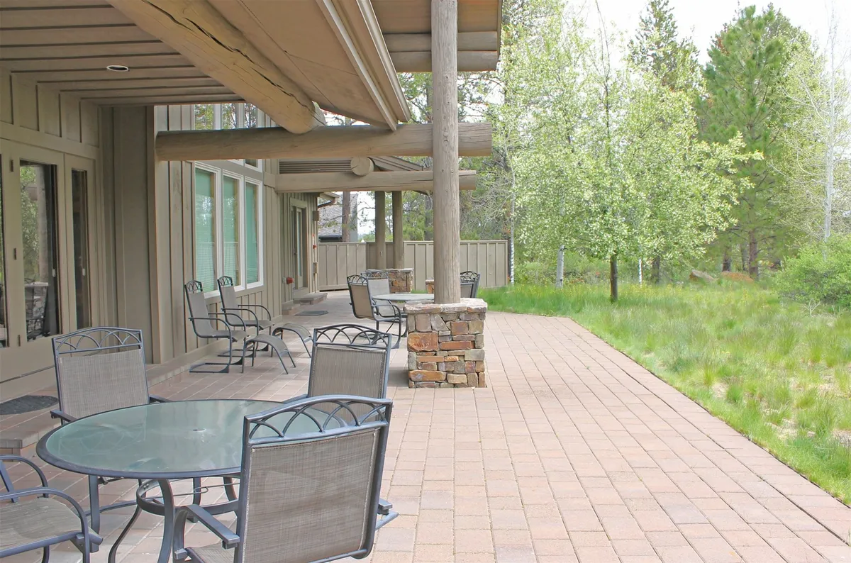 An expansive outdoor patio with comfortable seating and stone pillars, designed for hosting and relaxing. The patio is ideal for morning coffee or evening gatherings, with plenty of space for outdoor dining and socializing. The serene environment suggests a seamless extension of the home’s hospitality outdoors.