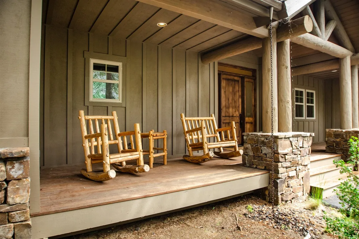 The exterior of the home featuring a welcoming front porch with rocking chairs and stone pillars, inviting relaxation. This space blends the boundary between indoors and outdoors, and beckons guests to enjoy quiet moments or social gatherings while taking in the natural surroundings, regardless of the season.