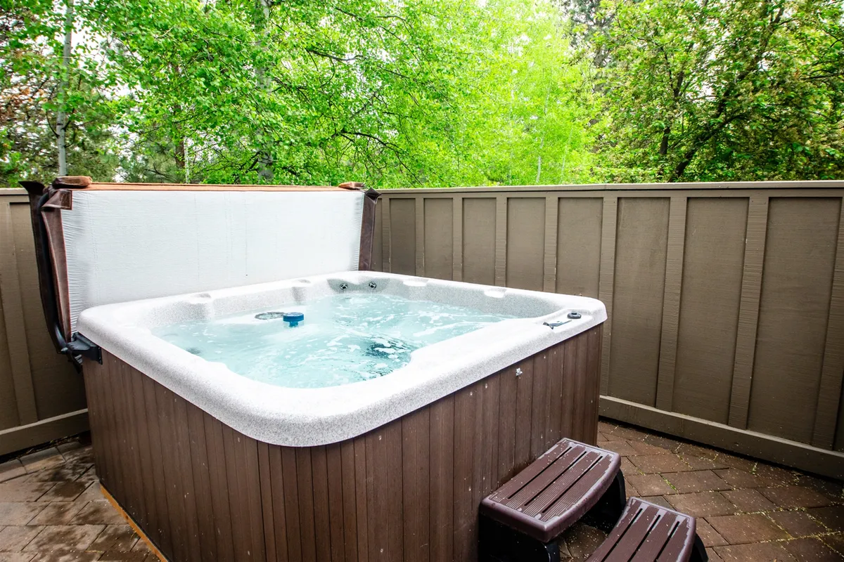A private outdoor hot tub nestled amid lush greenery and enclosed by a rustic fence, providing a tranquil setting for relaxation after an active day. The space is perfect for stargazing or enjoying a morning coffee in nature.