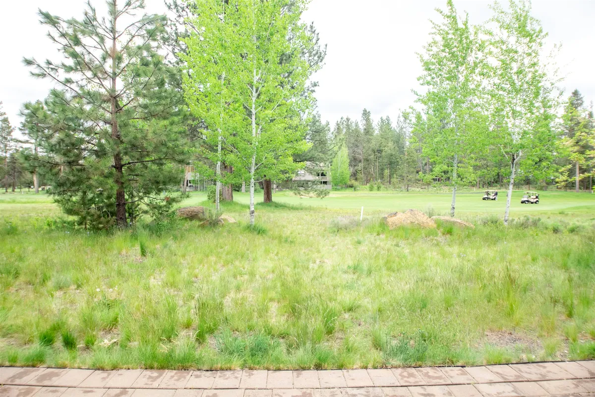 An exterior view showcasing a lush green golf course bordered by trees and open grassland. The tranquil scene is ideal for outdoor activities such as golfing, walking, or simply enjoying the panoramic views and wildlife sightings that define the summer experience in Sunriver.