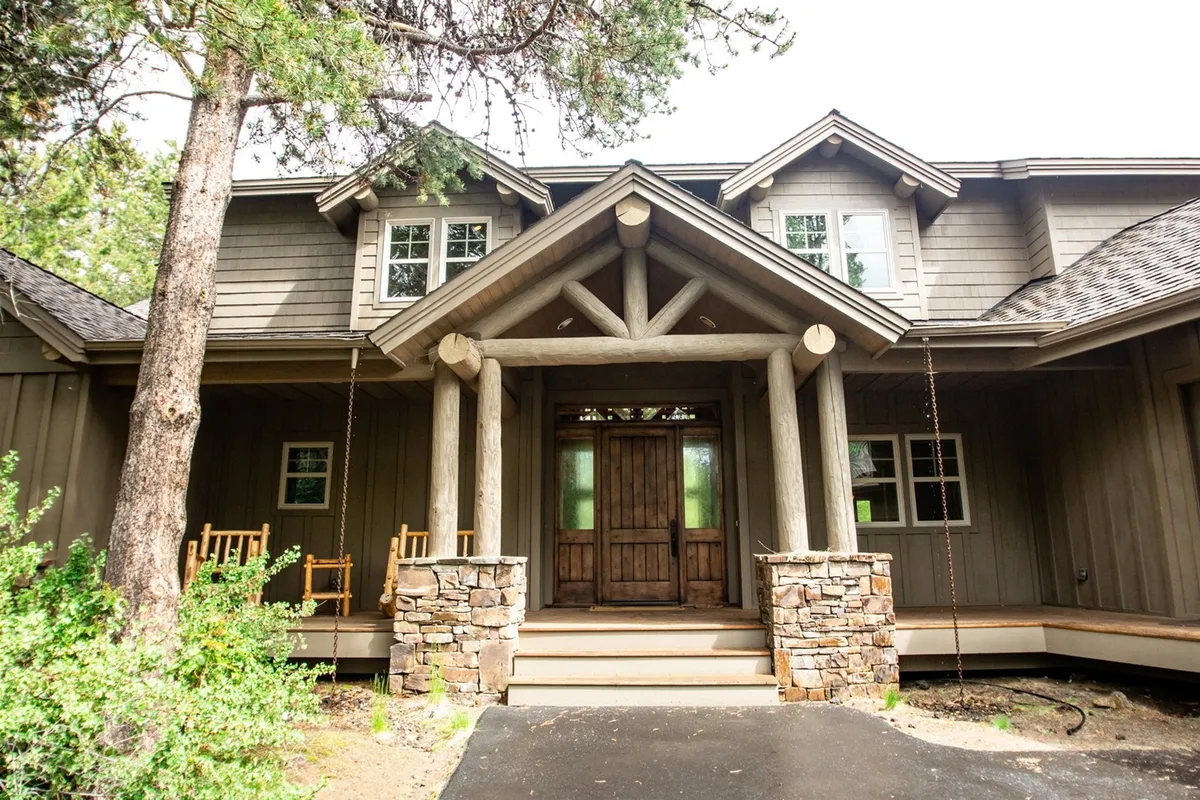 The welcoming front porch showcases sturdy stone pillars, a warm wooden door, and inviting rocking chairs—an ideal spot for relaxing, socializing, and connecting with nature.