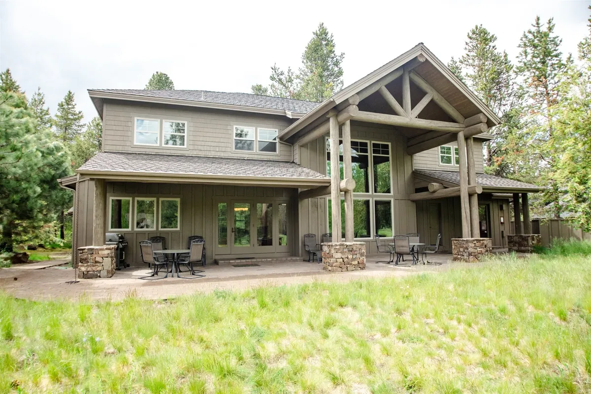 A spacious front porch with tall windows and natural stone features, surrounded by lush greenery. The inviting porch suggests a spot for outdoor dining, family gatherings, or simply enjoying the peaceful Sunriver environment.