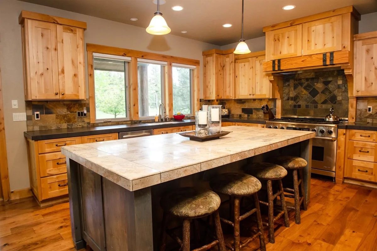 The gourmet kitchen is the focal point here, highlighted by a large kitchen island, warm wooden cabinetry, stainless steel appliances, and ample natural light streaming through nearby windows. The setup invites culinary creativity and social interaction, perfect for shared feasts or casual morning coffees.