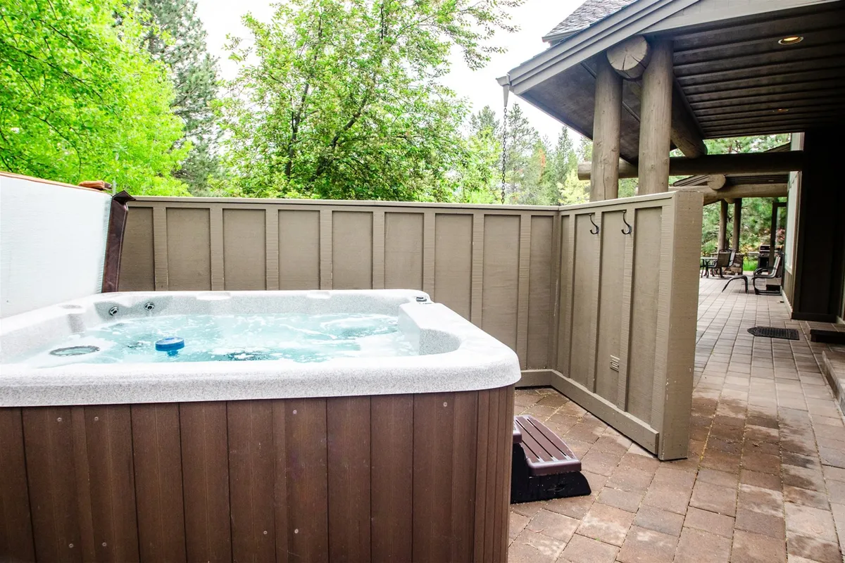 A tranquil patio scene featuring a private hot tub nestled amidst lush greenery. The patio area is designed for relaxation, with the hot tub being the main focal point. There is ample space around the tub for lounging and soaking in the surroundings, and the patio’s proximity to nature enhances the feeling of outdoor serenity.