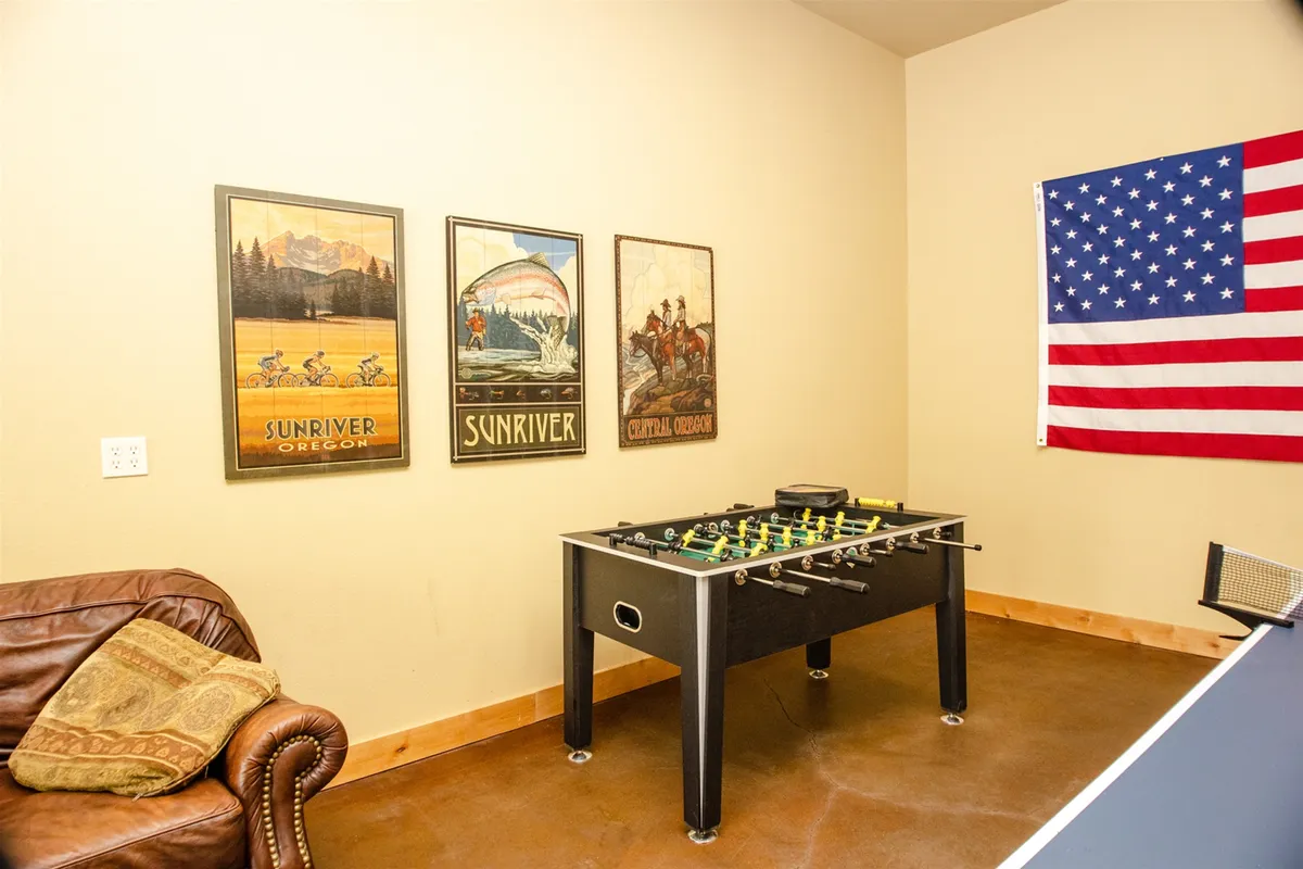 The game garage comes alive with a foosball table as its centerpiece, complemented by vintage posters, a comfy leather couch, and vibrant decor, creating a playful and social environment.