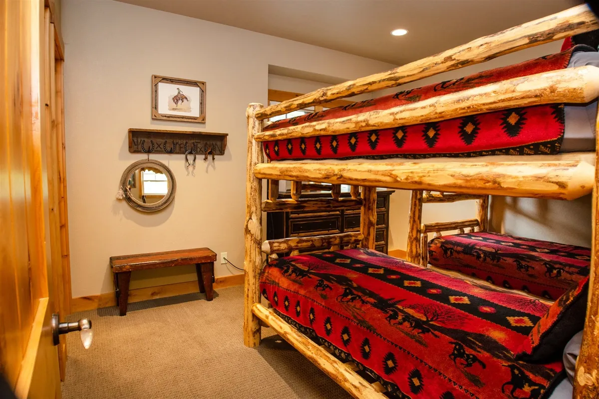 A cozy, inviting bunk room featuring wooden bunk beds, woven blankets, a decorative mirror, and a wooden bench. The space feels playful and communal, ideal for group sleepovers and kids’ adventures.